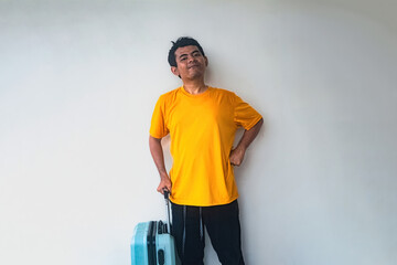 A traveler in a bright yellow shirt stands against a plain background, holding a blue suitcase. The image captures the essence of travel and adventure © Anzz Stock