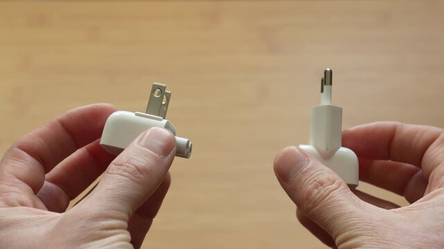 Close up front view of male hands holding US and European power plugs side by side. Concept of electrical standards, compatibility and international power connections.
