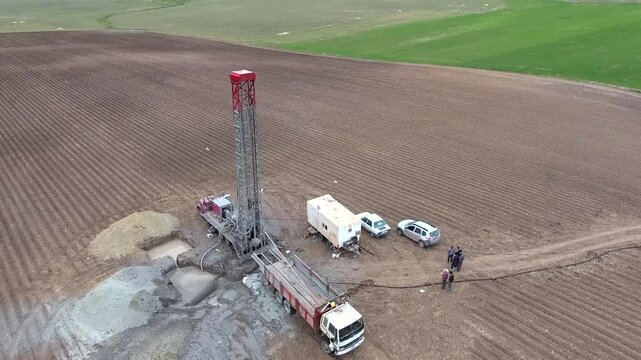 Workers drill a water well in farmland, surrounding the rig with trucks and field equipment. Borehole crew and rural machinery create an industrial agriculture scene with practical purpose.