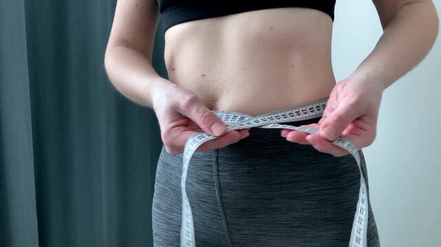 A woman measures her waist with a measuring tape. The idea of self-discipline, self-improvement, and the desire to achieve perfect proportions through sports, proper nutrition, and a mindful lifestyle