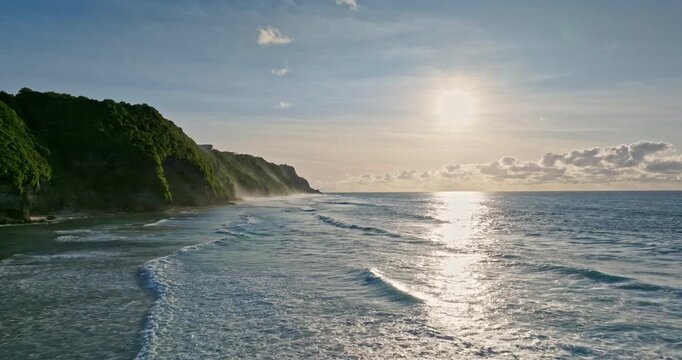 Tropical Bukit Peninsula cliffs receiving ocean waves under a dramatic sunset sky, creating a serene and vast shoreline landscape, perfect for travel and nature concepts. Aerial view drone flight