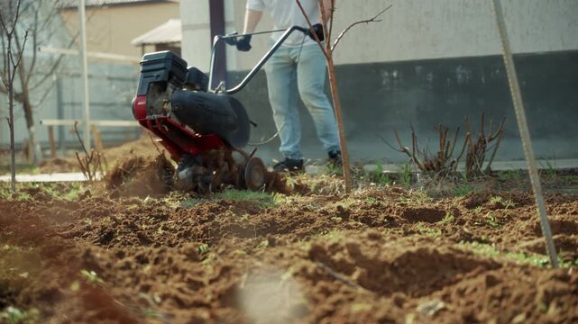 Man starting cultivator and plowing backyard soil