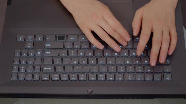A woman is actively typing on her laptop in a contemporary workspace, showcasing her focused engagement with technology during daytime hours.