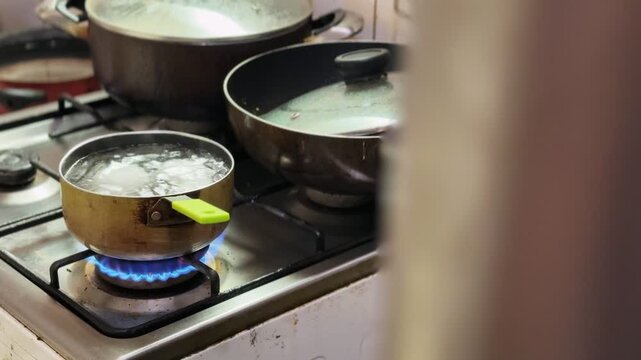 a blue gas flame heating a small pot of boiling water on a kitchen stove. Domestic cooking scene with background cookware and shallow depth of field. Ideal for culinary and energy ads.