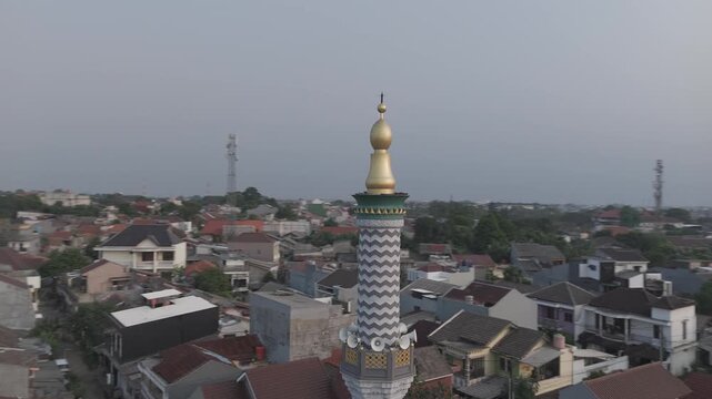 Shot in D-Log M for professional color grading Aerial drone point of interest shot circling a mosque minaret against a hazy sky at sunset.