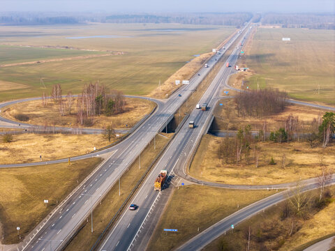 Aerial view of a highway interchange with trucks and cars driving through flat rural fields and bare trees Lithuania.