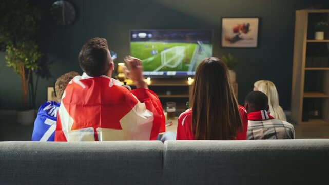 Group of Canadian football supporters watching live sports match on television at home while cheering for national team during championship tournament.