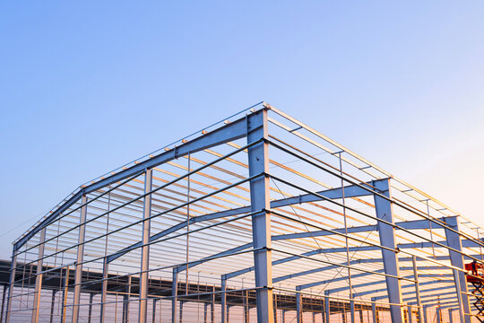 Metal columns structure and steel roof beam framework of industrial warehouse factory building in construction site against blue evening sky background, Low angle view