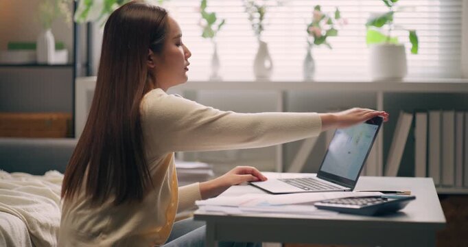 Exhausted young Asian female sleeping on table with laptop and document. Overwork, burnout, and fatigue from long hours of remote work in home office.