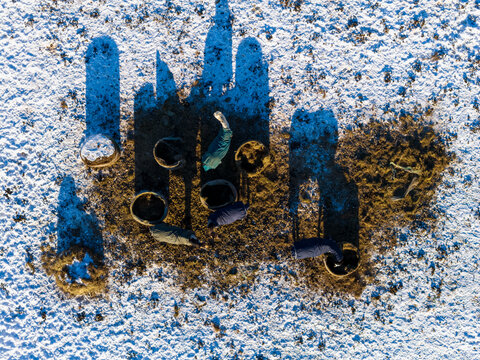 Aerial view of horses wearing blankets gathered around feeding troughs in a snowy field with long shadows Lithuania.