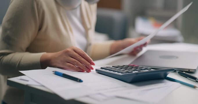 Close-up of female hand with pen writing on paper, using calculator with laptop on desk. Business, finance, accounting and tax planning at home or office.