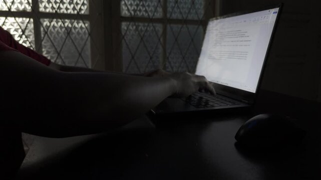 Shot in D-Log M for professional color grading Close up of male hands typing on a laptop keyboard in a dark room at twilight.