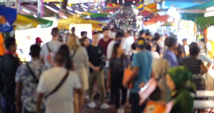 Slow motion defocused view of vibrant night market at Jalan Alor in Kuala Lumpur, with crowd of tourists walking along food stalls and restaurants. Lively atmosphere of this popular street at evening