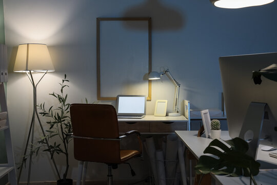 Interior of dark office with desks and glowing lamps at night