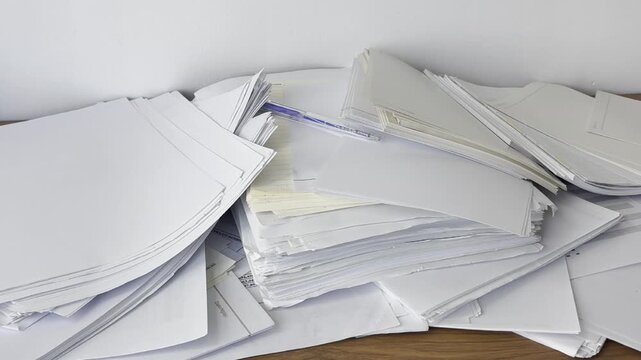 Video of scattered papers spread across a desk. Messy workspace scene representing stress, paperwork, office chaos, disorganization and busy work routine.