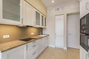 Fototapeta premium Stylish white kitchen set with built-in appliances. Beige countertop with sink and stove. The interior of an elegant kitchen.
