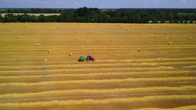 Tractor with baler gathers straw into bales. Mechanically baling straw for storage. Tractor working in field in summer and agricultural mechanization. Agricultural work after the grain harvest.