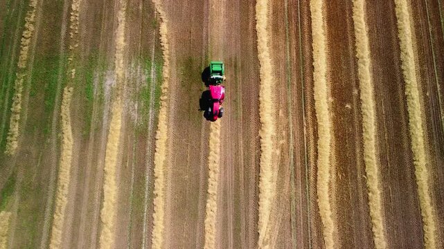 A tractor working in a field in summer. An overhead view of a tractor moving through rows of straw in agricultural land. Mechanized baling of straw for storage as livestock feed.