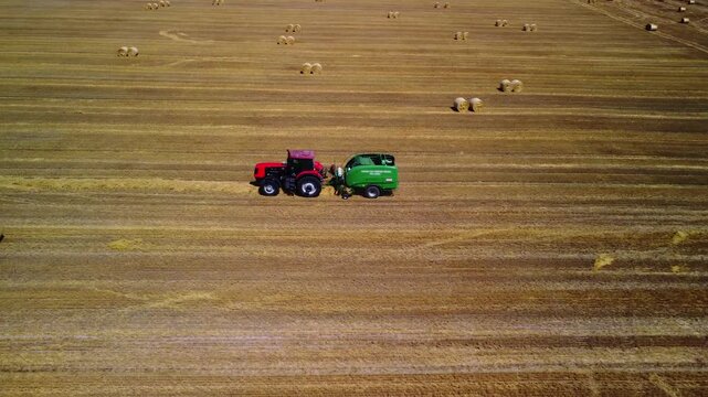 Tractor working in field in summer. Tractor pulls round baler. Agricultural process. Top view. Harvesting forage for cattle. Modern agriculture. Combination of tractor and baler works as single unit.