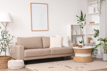 Naklejka premium Interior of light living room with sofa, blank frame and green plants