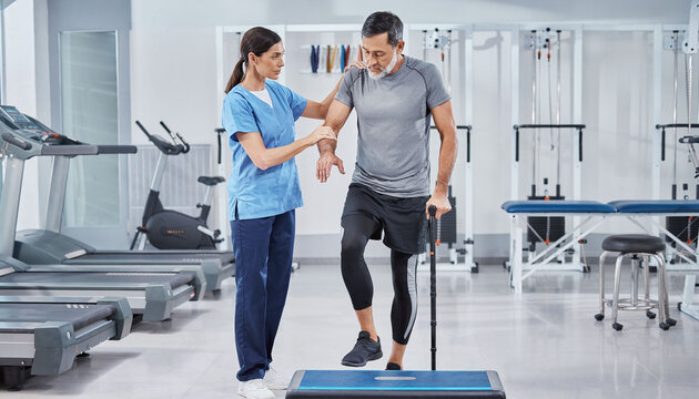 Professional physiotherapist guiding a senior man through rehabilitation exercises on a step platform, representing strength, recovery, and expert care in a modern clinical fitness gym.