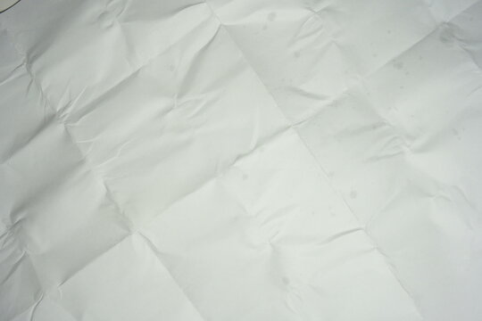 Texture of crumpled and folded white paper. Background of messy creased paper sheet with grid lines from folding, top view surface texture.