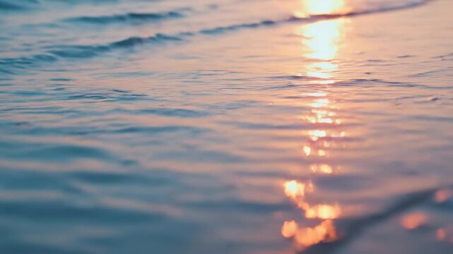 Slow motion tracking shot of shallow ocean waves gently lapping and retreating over wet sandy shore reflecting sunset light, close up coastal shoreline study