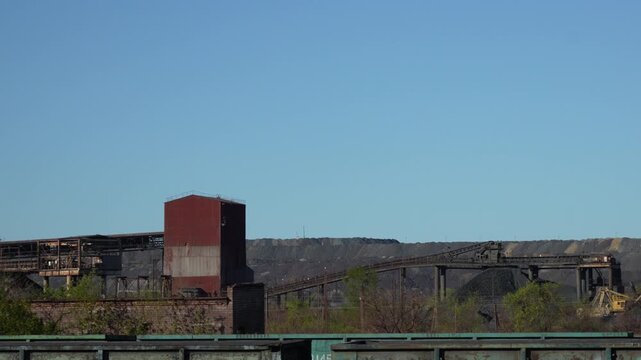 Industrial mining landscape with waste rock heaps, factory infrastructure and industrial buildings in background. Horizontal camera movement across post industrial area in 4K.