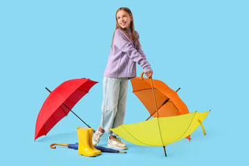 Obraz premium Cute teenage girl with different umbrellas and rubber rain boots on blue background