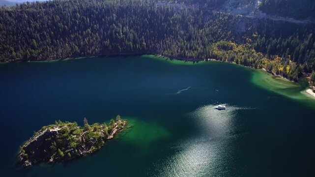 Cinematic aerial view of a mountain lake with a boat creating wake trails and sunlight reflecting on the surface.