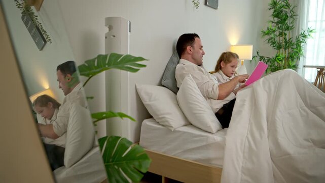 Father  reading a bedtime story together to daughter on the bed with funny facial expressions in a cozy bedroom