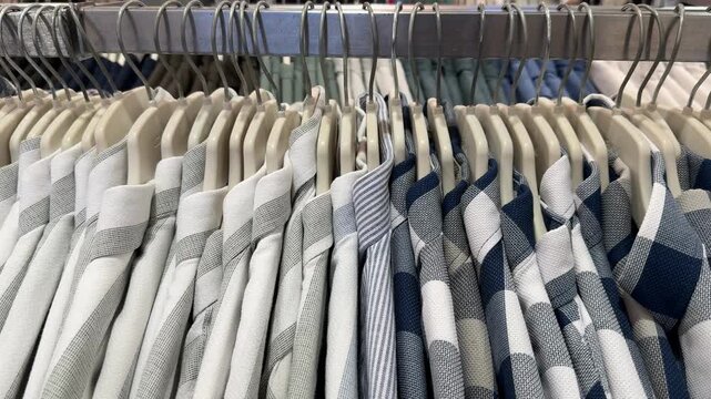 Rack of neatly arranged mens plaid and striped shirts in retail clothing store setting
