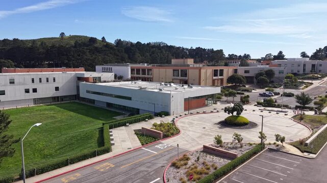 Afternoon aerial perspective showing the modern architecture of Skyline College in San Bruno, California, on a sunny day with green lawns and surrounding hills. Zoom in shot filmed in 4K
