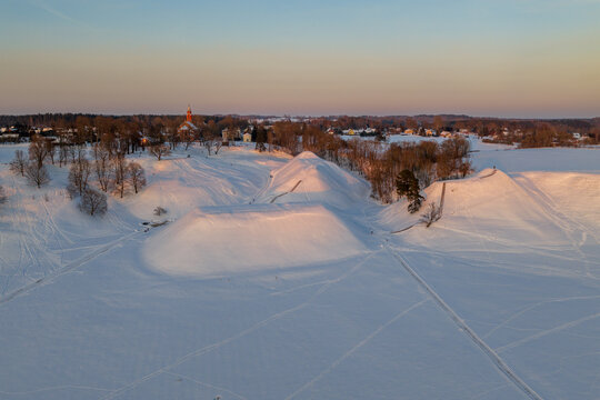Aerial view of the snow-covered Kernave Archaeological Site mounds during golden hour with a church in the background Kernave, Vilnius County, Lithuania.