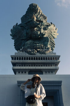 Female tourist in hat posing in front of the Garuda Wisnu Kencana statue in Bali, Indonesia, famous cultural landmark and travel destination.
