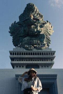Female tourist in hat posing in front of the Garuda Wisnu Kencana statue in Bali, Indonesia, famous cultural landmark and travel destination.