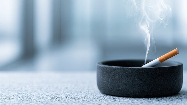 Lit cigarette smoldering in a dark ashtray, wisps of smoke rising gently