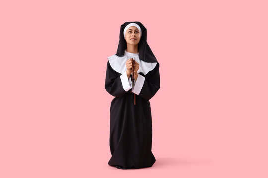Young nun with beads praying on pink background