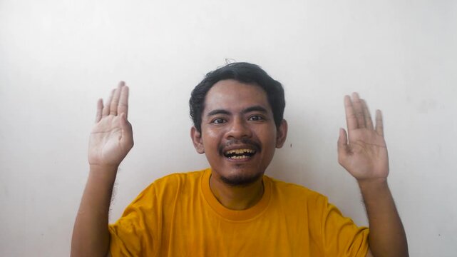 Excited young man with wide smile and raised hands celebrating a victory or good news in studio