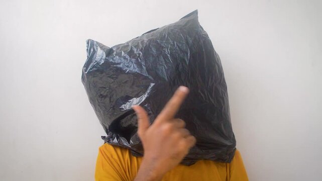 Man with black plastic bag over head making rock on gesture against white wall background