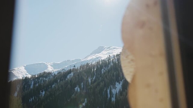 Snowy alpine mountain range with pine forests seen from a rustic wooden cabin on a bright sunny day