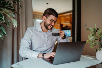 Man smiling working remotely on laptop drinking coffee