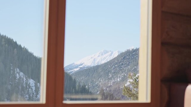 Beautiful snowy mountain and pine forest landscape seen from the window of a rustic wooden log cabin