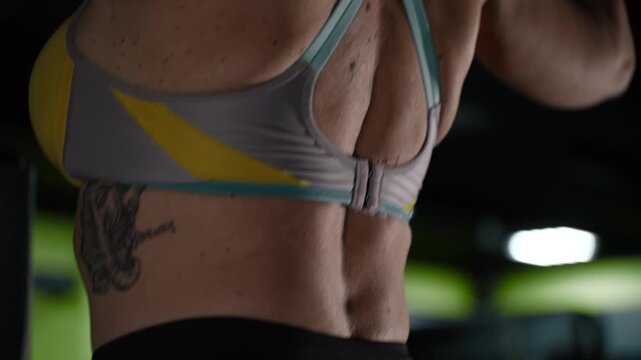 Close-up of woman in top exercising in gym in the evening. Back and arm exercises on machine for women.