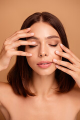 Naklejka premium Close up portrait of a young woman with polished makeup and relaxed expression showcasing beauty and skincare in a warm beige studio backdrop