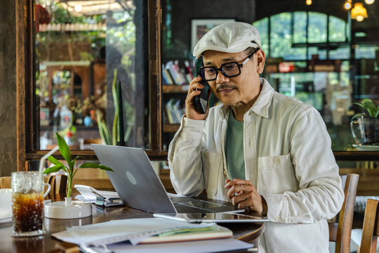 Senior Cafe small business entrepreneur reviewing documents beside laptop digital workflow managing finance and accounting tasks modern management technology improving efficiency and organization