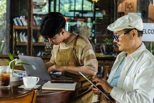 Modern family small business digital management, senior cafe owner guiding young barista worker or son sharing experience teamwork learning growth trust technology management lifestyle in coffee shop