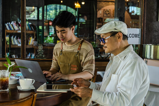 Modern small business digital technology, father and son cafe owner, young entrepreneur management, using laptop and tablet planning orders finance workflow efficiency technology business operation