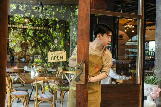 Small business cafe restaurant owner entrepreneur managing storefront with open or closed sign, young barista working daily routine with customer interaction, business operation in local coffee shop