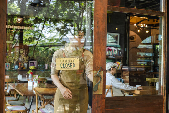 Young barista cafe owner flipping sign to open on storefront door, welcoming customers with confident smile, small business startup energy and positive service mindset in hospitality environment.